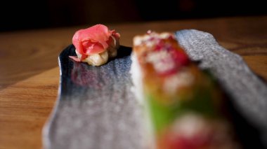 Ahşap masa, foodporn kavramı üzerinde duran siyah bir tabak üzerinde Japon suşi rulo için yakın. Çerçeve. Sos ve havyar ile süslenmiş taze lezzetli rulolar.