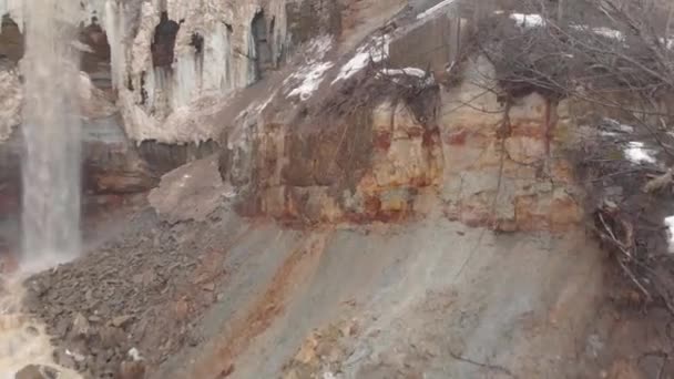 Gros plan de petites chutes d'eau sur les couches de falaises brunes couvertes de glace et de neige. Des actions. Début du printemps — Video