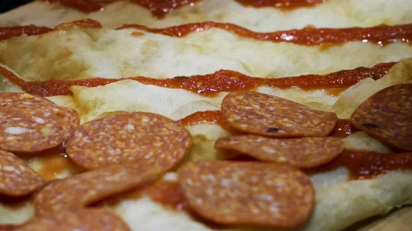 Close up para salame de pizza enquanto o processo de preparação, conceito de cozinha. Moldura. Chef mãos em luvas pretas colocando salame na pizza antes de assar . — Fotografia de Stock