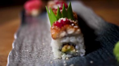 Ahşap masa, foodporn kavramı üzerinde duran siyah bir tabak üzerinde Japon suşi rulo için yakın. Çerçeve. Sos ve havyar ile süslenmiş taze lezzetli rulolar.