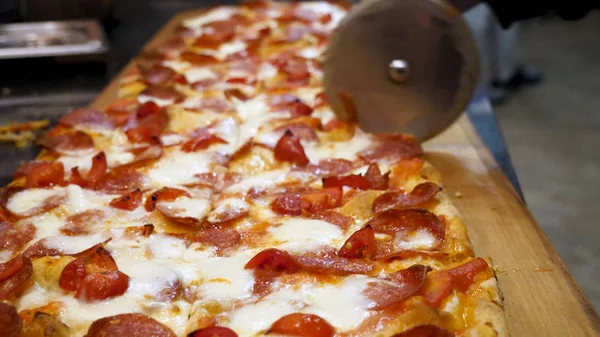 Close up for hands of chef baker in black cooking gloves cutting pizza at the kitchen, delicious italian food concept. Frame. Man cuts freshly prepared pizza slices with a special knife. — Stock Photo, Image