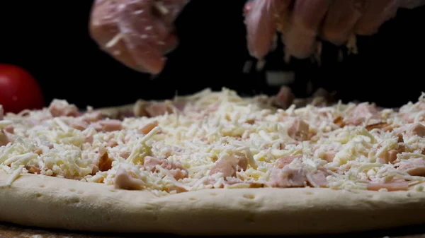 Женские руки в перчатках для приготовления пиццы с тертым сыром, итальянская концепция питания. Рамка. Закрыть для повара руки положить сыр на пиццу . — стоковое фото