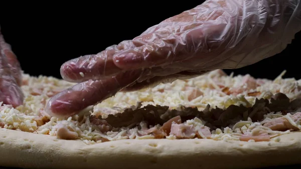 Närbild för chef händer i transparenta handskar röra unugnsbakad pizza på svart bakgrund, Matlagning koncept. Ram. Man i matlagning handskar förbereder pizza för bakning. — Stockfoto