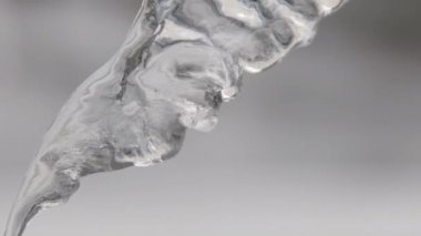 Bulanık gri arka plana doğru akan damlacıklarla eriyen buz sarkıtlarını asmak için kapatın. Stok görüntüleri. İlkbaharda güzel berrak buz sarkıtı parıldama ve erime.