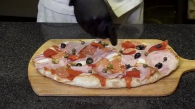 Siyah pişirme eldivenşef pizza ahşap bir tahta, lezzetli yemek konsepti üzerinde yalan yapıyor. Çerçeve. Pizzanın üzerine zeytin ve mozarella koyarak eller için kapatın.