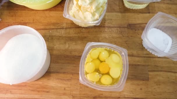 Draufsicht auf die Zutaten für Gebäck: Mehl, Eier, Milch und Zucker vor einem hölzernen Hintergrund. Archivmaterial. Küchentisch mit den Zutaten in Plastikbehältern. — Stockvideo