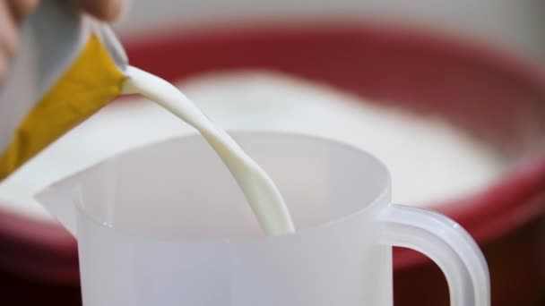Verser du liquide blanc dans une tasse à mesurer avec un récipient de farine sur le fond, concept de cuisson. Images d'archives. Lait versé dans une tasse à mesurer en plastique .
