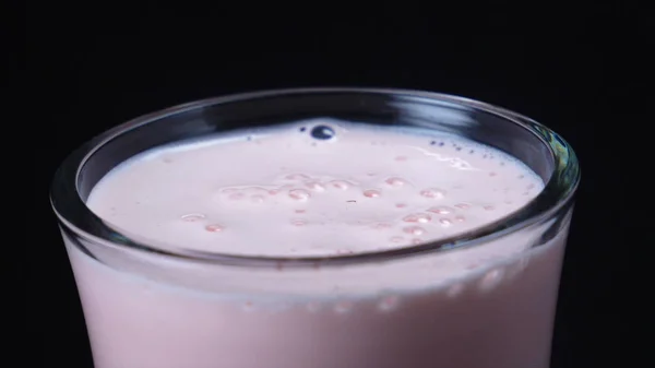 Close-up de vidro transparente de milkshake de morango com grande morango caído vermelho no fundo preto. Moldura. Coquetéis com leite e bagas — Fotografia de Stock