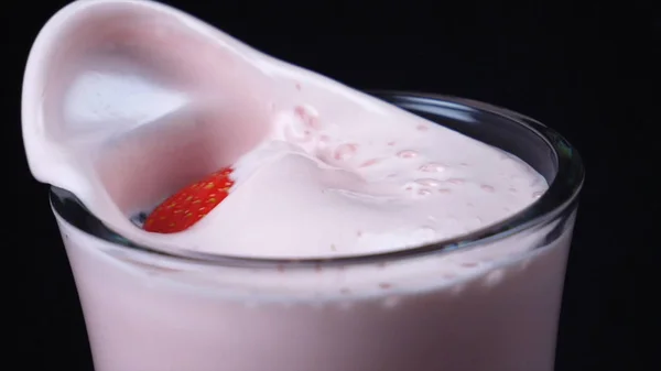 Крупный план прозрачного стакана клубничного молочного коктейля с большой красной упавшей клубникой на черном фоне. Рамка. Коктейли с молоком и ягодами — стоковое фото