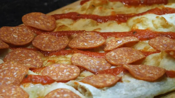 Close-up de chefs mãos em luvas de proteção pretas cobrindo a massa de pizza com grandes fatias de salame em uma tábua de madeira. Moldura. Fabricação de pizza tradicional italiana — Fotografia de Stock