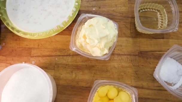 Draufsicht auf die Zutaten für Gebäck: Mehl, Eier, Milch und Zucker vor einem hölzernen Hintergrund. Archivmaterial. Küchentisch mit den Zutaten in Plastikbehältern. — Stockvideo