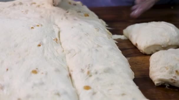 Close-up voor de vrouw in koken handschoenen snijden van het deeg in stukken met een speciaal mes. Stock footage. Vrouwenhanden knippen de rauwe gekneden deeg in stukken op houten plank. — Stockvideo