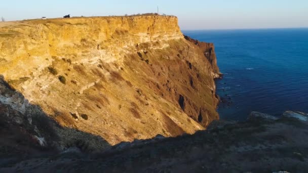 Top view of coastal cliff with blue sea at sunset. Shot. Beautiful view of golden sunset light on rocky cliffs of sea coast with blue waters — Stock Video