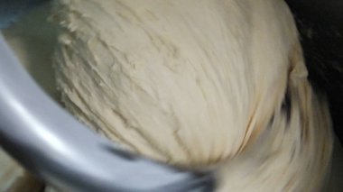 Close-up of dough mixing in a professional kneader machine in kitchen of bakery or at the manufacturing. Stock footage. Dough making process