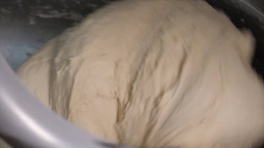 Close-up of mixing a dough for bread baking or other baked goods in a professional kneader machine in kitchen of bakery or at the manufacturing. Stock footage. Dough making process