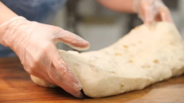 Крупный план рук пекаря в перчатках с использованием кухонной утвари и нарезанием теста на кухне в пекарне. Запись. Подготовка выпечки — стоковое фото