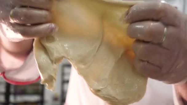 Cierre para arriba para una mujer que estira la masa cruda usando sus manos en guantes de cocina en la panadería. Imágenes de archivo. Manos femeninas sosteniendo y estirando pastelería cruda . — Vídeo de stock