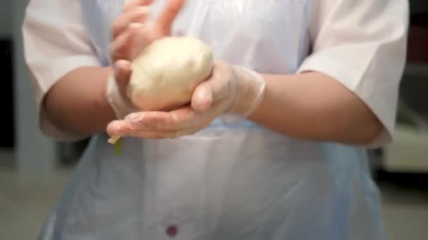 Chiudere per una donna che tiene un pezzo di pasta cruda con le mani in guanti da cucina presso la panetteria. Filmati delle scorte. Mani femminili fanno una palla da pasticceria cruda . — Video Stock