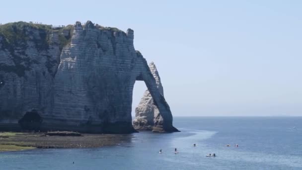 Beautiful view of rocky beach with tourists and surfers. Action. Cliffs with beach by blue sea with bunch of tourists on summer vacation engaged in surfing and swimming — Stock Video