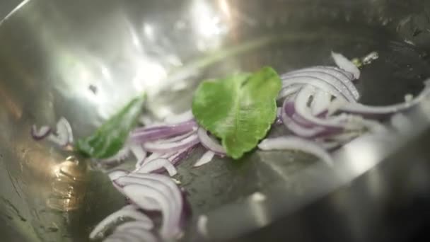 Close-up van het roosteren van uien in pan. Actie. Koken begint met het roosteren van uien gekruid met laurierblaadjes voor piquancy. Professionele koekenpan gebruikt in de keuken — Stockvideo