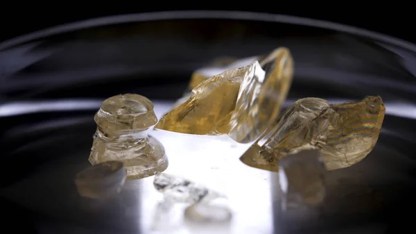 Прекрасные минералы разного размера лежат в чашке Петри на черном столе, научная концепция. Запись. Желтые кристаллы лежат на стеклянной подставке, концепция химии . — стоковое фото