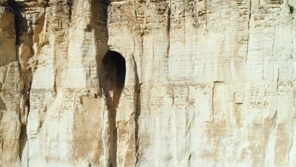 Крупный план рельефа белого склона скалы с большим отверстием или гротом в середине склона. Выстрел. Таинственная пещера в скале — стоковое видео