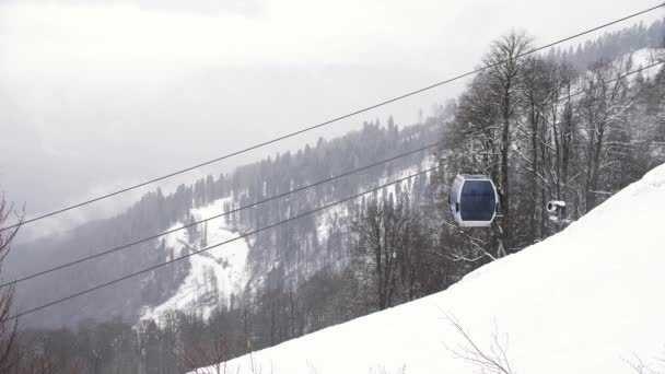 बर्फीले पेड़ों से ढकी हुई पहाड़ी ढलान के साथ शीतकालीन परिदृश्य और चलती केबिनों, स्की रिसॉर्ट के साथ फ्यूनिक्यूलर। कला। ग्रे आकाश पृष्ठभूमि पर घाटी पर स्की केबल कार . — स्टॉक वीडियो
