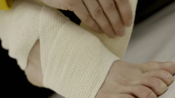 Close-up woman bandaging her leg with elastic bandage. Action. Unexpected injury or stretching of ankle while exercising and applying elastic bandage