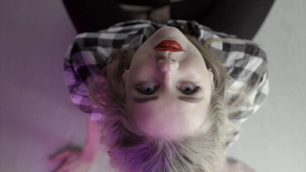 Young woman looks tilting back her head. Action. Young attractive woman looks back with her head straight into camera upstairs. Frightening look of woman straight up