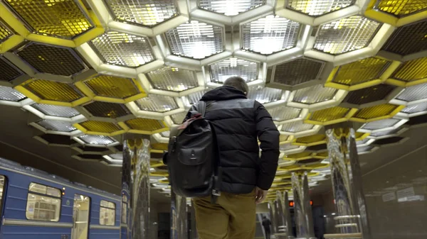 Young man with backpack walking on subway. Action. Rear view of attractive young man walking on subway on background of designer ceiling with honeycombs — Stock Photo, Image