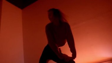Genç ve çekici bir kadın karanlık odada dans ediyor. Başla. Profesyonel dansçı, loş bir odada modern tarzda canlı ve tutkulu bir şekilde dans ediyor.