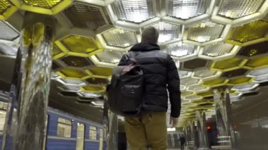 Sırt çantalı genç adam metroda yürüyor. Başla. Metroda yürüyen çekici bir gencin arka plandaki tasarımcı tavanında bal peteğiyle yürümesi.