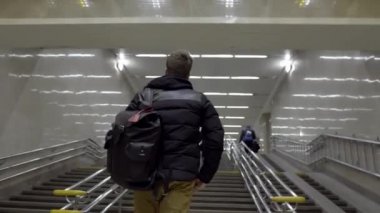 Metroda sırt çantalı genç bir adam var. Başla. Kapalı fayanslı odada, geniş merdivenlerden çıkan genç adamın arka görüntüsü.