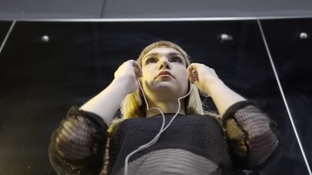 Jeune femme portant de petits écouteurs. L'action. Vue du bas de la jeune femme attrayante épique portant des écouteurs avec de la musique avant la performance — Video