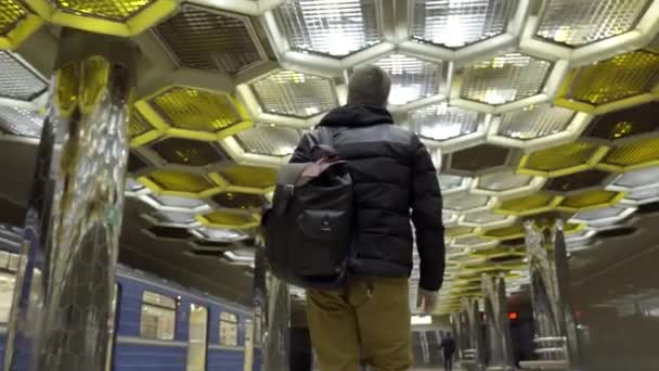 Jeune homme avec sac à dos marchant dans le métro. L'action. Vue arrière d'un jeune homme séduisant marchant dans le métro sur fond de plafond design avec nids d'abeilles — Video