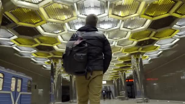 Jongeman met rugzak loopt met de metro. Actie. Achteraanzicht van aantrekkelijke jonge man lopen op metro op de achtergrond van designer plafond met honingraten — Stockvideo