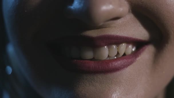 Close-up of smile woman with red lips on dark background. Action. Mesmerizing and frightening smile of woman with red lipstick on dark background with cold lighting — Stock Video