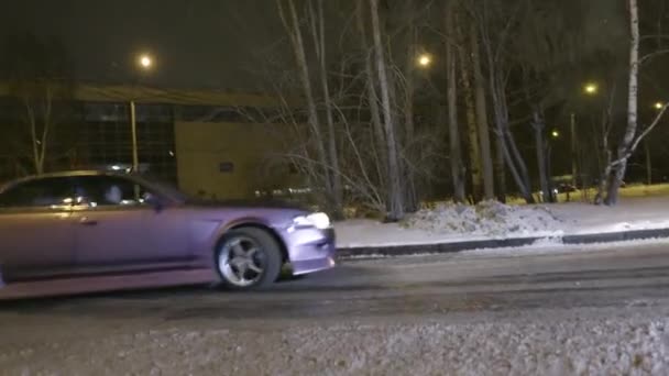 El coche se desplaza por la carretera cubierta de nieve en la ciudad nocturna. Acción. Elegante coche nuevo gira bruscamente a su vez en la carretera cubierta de nieve en la ciudad — Vídeos de Stock