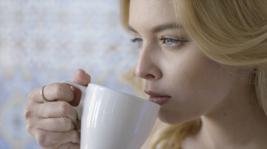Güzel mavi gözlü genç sarışın kadın çay içiyor. Eylem. Parmağında yüzük ile genç güzel bayan beyaz kupa dan kokulu sıcak çay içme