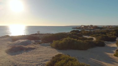 Deniz ve mavi gökyüzü arka planda Bushy plaj. Madde. Yeşil çalılar ve güneşi yansıtan sessiz deniz ile güzel plajın üst görünümü