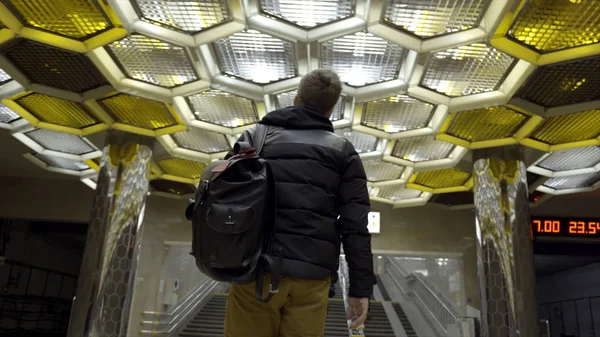 Rear view of young man walking in subway. Action. Traveler goes with backpack on subway on background of designer ceiling with honeycombs. Beautiful design metro finish — Stock Photo, Image