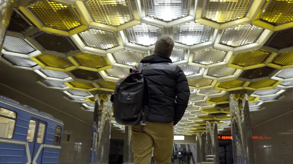 Rear view of young man walking in subway. Action. Traveler goes with backpack on subway on background of designer ceiling with honeycombs. Beautiful design metro finish — Stock Photo, Image