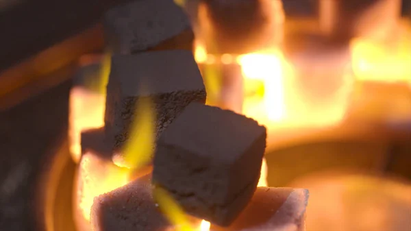 Close-up of burning charcoal cubes. Action. Cubes of embers burning in bowl for smoking hookah. Combustion of small flame of yellow fire burning pieces of coal