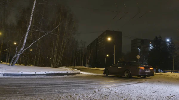 Car drifts on snow-covered road in night city. Action. Stylish new car turns sharply on turn on snow-covered road in city