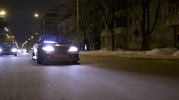 Vista inferiore di auto cool guida sulla città di notte. Azione. Brillante finitura oro scuro con brillantini sulla guida in auto attraverso la città di notte e scintillante dalla luce delle lanterne — Foto Stock