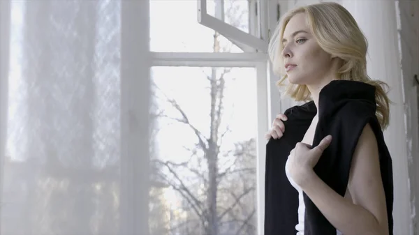 Beau fond blond aux yeux bleus de fenêtres blanches. L'action. Belle jeune femme regarde quelque chose sur fond de fenêtres claires avec du tulle blanc en développement — Photo