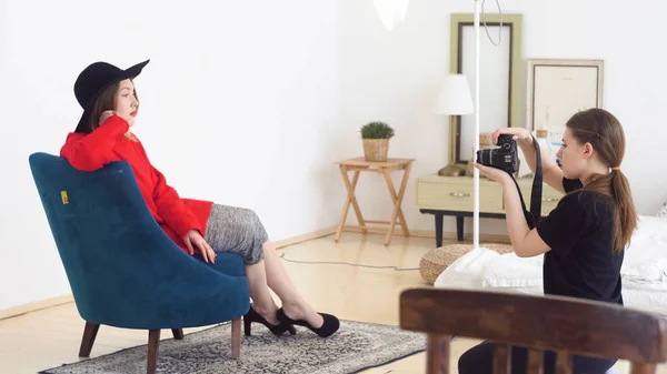 La mujer es fotógrafa y modelo durante el rodaje. Medios. Fotógrafo endereza su sombrero en modelo femenino atractivo sentado en la silla antes de disparar en el estudio de fotos —  Fotos de Stock