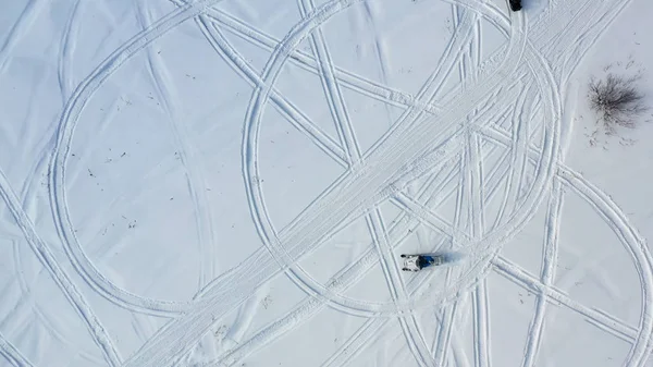 Вид сверху на катание на снегоходах. Запись. Вид сверху на два снегохода, едущих по кругу, оставляя следы на снегу в солнечный день — стоковое фото