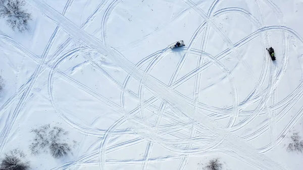 Vista superior de motos de nieve. Filmación. Vista superior de dos motos de nieve conduciendo en círculo dejando huellas en la nieve en un día soleado — Foto de Stock