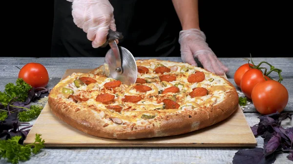 Кук режет пиццу роллерножом. Рамка. Шеф-повар перчатки вырезать роллер нож свежеиспеченные пиццы. Резка вкусной пиццы перед подачей — стоковое фото